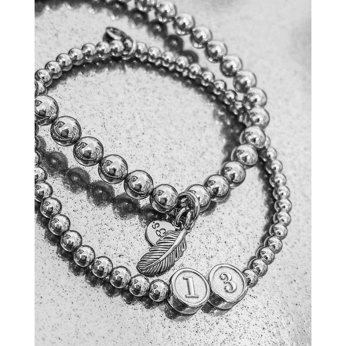 zwei auf glänzendem Untergrund liegende Armbänder mit Kugeln und Federanhänger und Kugeln und  den Ziffern 1 und 3 auf Buchstabenperlen von strawberry & cream